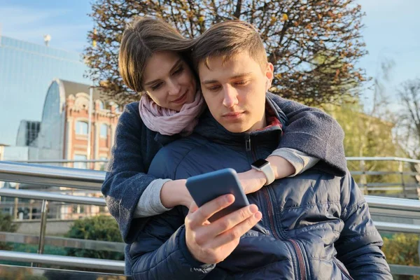 Pareja joven leyendo texto en el teléfono, fondo de la ciudad de primavera —  Fotos de Stock