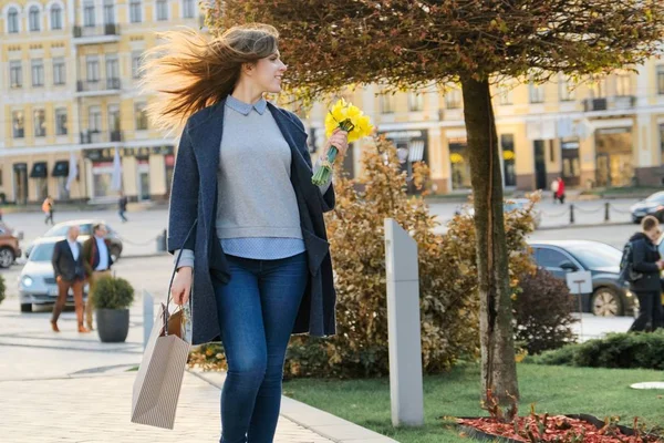Портрет красивой девушки, гуляющей по городу, молодая женщина с букетом желтых цветов и сумки, фон весенний город — стоковое фото