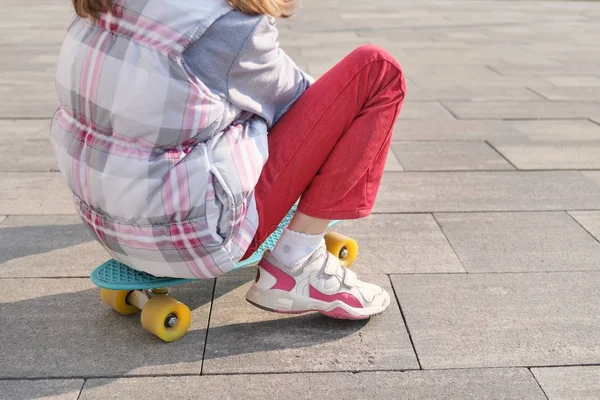 Little girl rides a skateboard, in area near the house, spring season, gray wall background — Stock Photo, Image