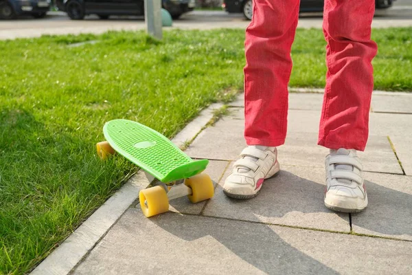 Perder-up de pernas meninas e skate, fundo é cinza pedras de pavimentação e grama verde no quintal . — Fotografia de Stock