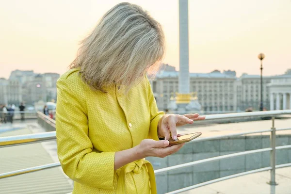 Открытый портрет зрелой женщины со смартфоном, пальцы на сенсорный экран, текстовое сообщение, пространство для копирования, золотой час — стоковое фото