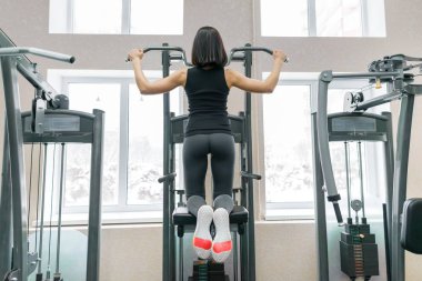 Spor salonundaki spor makinesinde sırtı için egzersiz yapan genç bir kadın, arkadan gören bir kadın. Fitness, spor, eğitim, insan konsepti