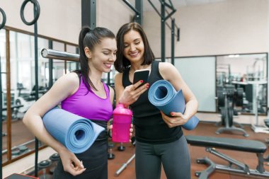Spor salonunda Spor paspaslar ile konuşurken fitness kadınlar gülümseyen iki genç. Eğitim, takım çalışması, sağlıklı yaşam konsepti.