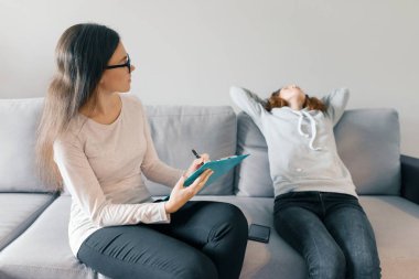 Profesyonel çocuk psikoloğu ofiste genç kız ile konuşurken, kız kanepede oturan