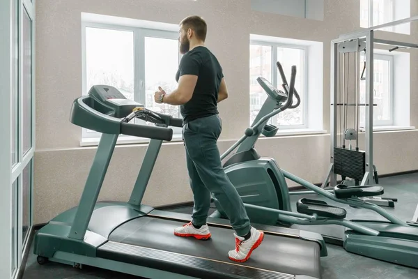 运动肌肉胡子男子在现代运动健身房的跑步机上跑步。健身、运动、训练、人的概念 — 图库照片