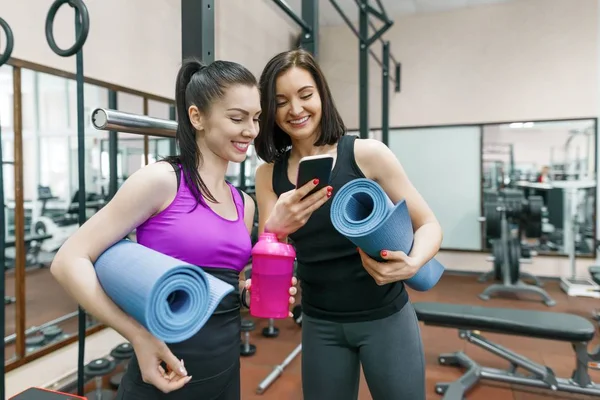 Duas jovens mulheres de fitness sorrindo conversando com tapetes esportivos no ginásio. Treinamento, trabalho em equipe, conceito de estilo de vida saudável . — Fotografia de Stock