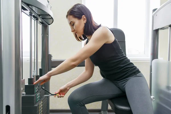 Giovane donna atletica che esercita sulle macchine in palestra sportiva moderna. Fitness, sport, allenamento, persone, concetto di stile di vita sano . — Foto Stock