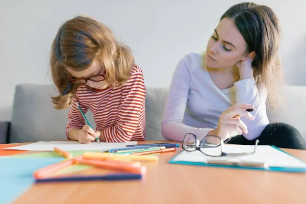 Junge Lehrerin gibt Kind Privatunterricht, kleines Mädchen sitzt am Schreibtisch und schreibt in Notizbuch — Stockfoto