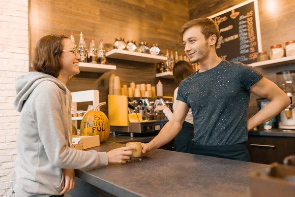 Jovem sorridente barista masculino vendendo bebida para uma adolescente na cafeteria — Fotografia de Stock