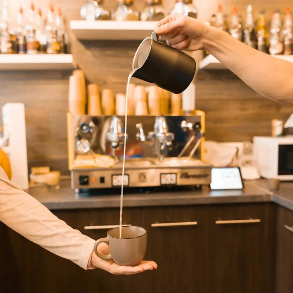 Closeup of pouring steamed milk into coffee cup, coffee shop background — Stock Photo, Image