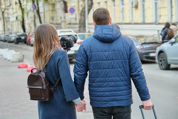 Τουρίστες νεαρό ζευγάρι περπάτημα γύρω από την πόλη με βαλίτσα κάμερα, θέα από την πλάτη, ταξίδια νεολαίας, χειμερινή εποχή της άνοιξης. — Φωτογραφία Αρχείου