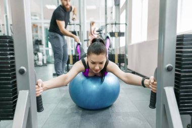 Kinezis teknolojisi, kinesiterapi, sağlıklı yaşam tarzı. Genç kadın kinesi makine, fitness spor salonu arka plan kullanarak kişisel eğitmen ile rehabilitasyon egzersizleri yapıyor