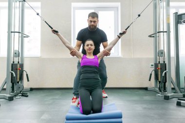 Kinezis teknolojisi, kinesiterapi, sağlıklı yaşam tarzı. Genç kadın kinesi makine, fitness spor salonu arka plan kullanarak kişisel eğitmen ile rehabilitasyon egzersizleri yapıyor