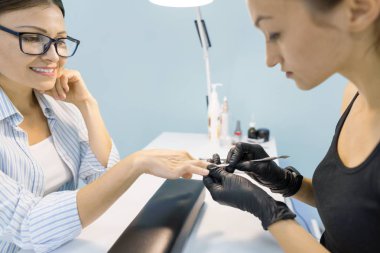 Genç kadın Güzellik Güzellik tırnak salonu profesyonel araçlar ile manikür yaparken içinde gülümseyen, tırnak ve el Bakımı