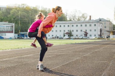 Spor neşeli aile, sağlıklı yaşam tarzı, anne ve küçük kızı eğlenceli ve stadyumda çalışan bahar portresi
