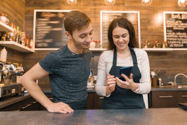 Kahve Dükkanı erkek ve kadın barın arkasında genç işçiler sayaç, smartphone bakarak konuşuyor