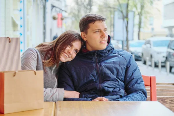 Jovem casal sorrindo com sacos de compras no café da rua, esperando por xícara de café e chá — Fotografia de Stock