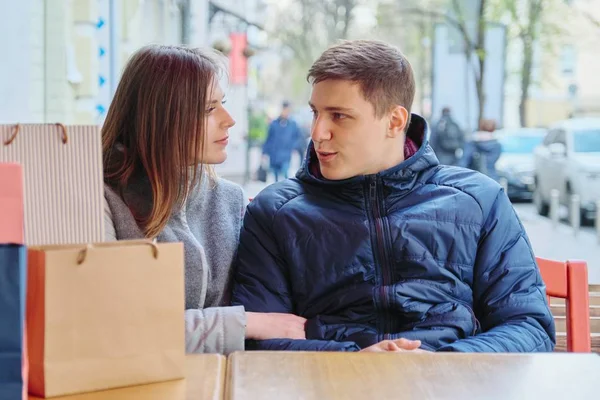 Young talking couple with shopping bags in street cafe, waiting for cup of coffee and tea — Stock Photo, Image