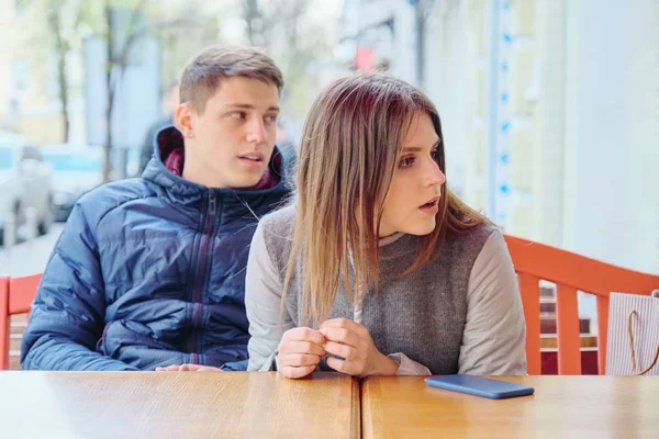 Emotional surprised young couple in outdoor cafe, sitting at the table