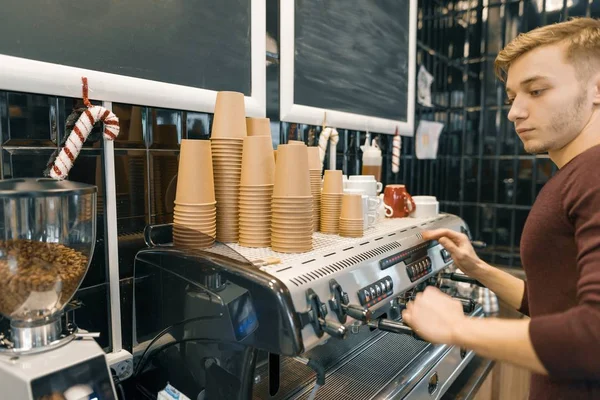 若い男性のバリスタがコーヒーマシンの近くで飲み物を作ります。コーヒーショップ事業コンセプト — ストック写真