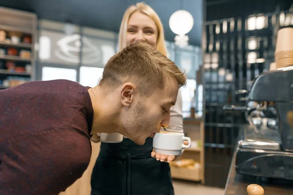 Jeune homme appréciant le café parfumé frais, boire du café dans une tasse dans les mains de fille barista — Photo