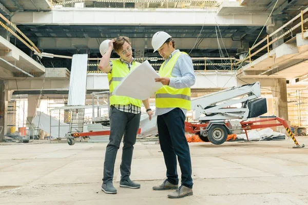 Trabajadores de la construcción masculinos que trabajan en el sitio de construcción, constructores que buscan en el plano. Construcción, desarrollo, trabajo en equipo y concepto de personas — Foto de Stock