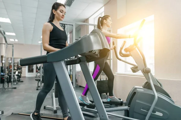 Dos mujeres jóvenes fitness saludable en la cinta de correr en el deporte moderno gimnasio. Fitness, deporte, entrenamiento, concepto de personas . — Foto de Stock