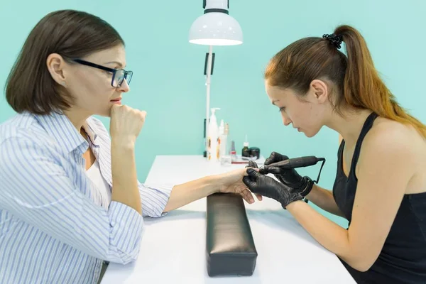 Jovem esteticista no salão de beleza fazendo manicure com ferramentas profissionais, cuidados com as unhas — Fotografia de Stock