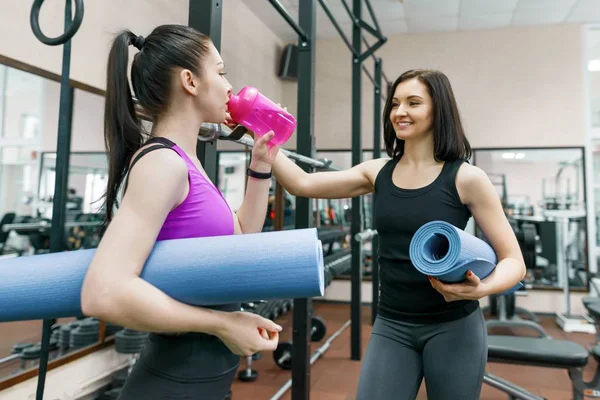 Zwei junge lächelnde Fitness-Frauen im Gespräch mit Sportmatten in der Turnhalle. Training, Teamwork, gesundes Lebensstilkonzept. — Stockfoto