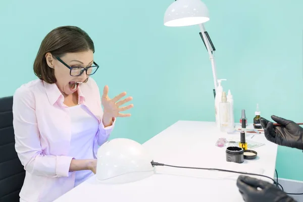 Manicurist uses an ultraviolet lamp for fixing gel nail polish. A woman screams from the pain to her nails under the lamp