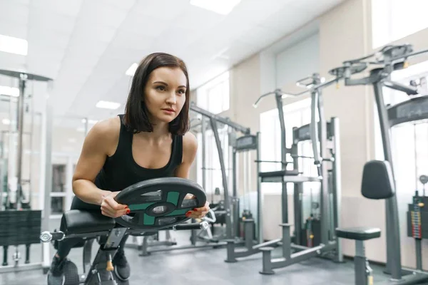 Mujer atlética joven haciendo ejercicio en las máquinas en el gimnasio deportivo moderno. Fitness, deporte, entrenamiento, personas, concepto de estilo de vida saludable . — Foto de Stock