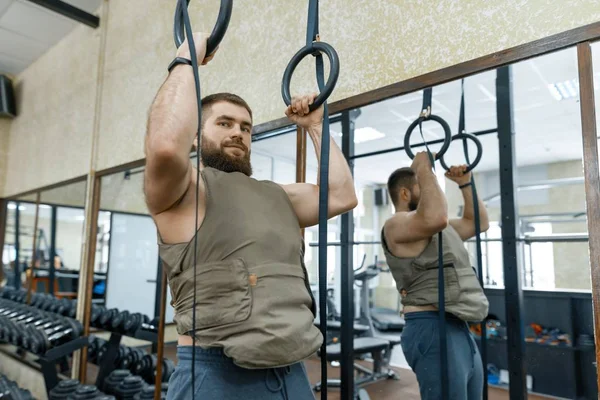 Kas beyaz sakallı adam egzersizleri yapıyor spor salonunda, askeri tarzı ağırlıklı yelek giymiş — Stok fotoğraf