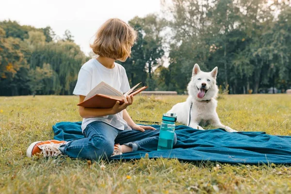 Petite fille avec chien blanc Husky dans le parc s'assoit sur l'herbe, joue, lit, se repose — Photo