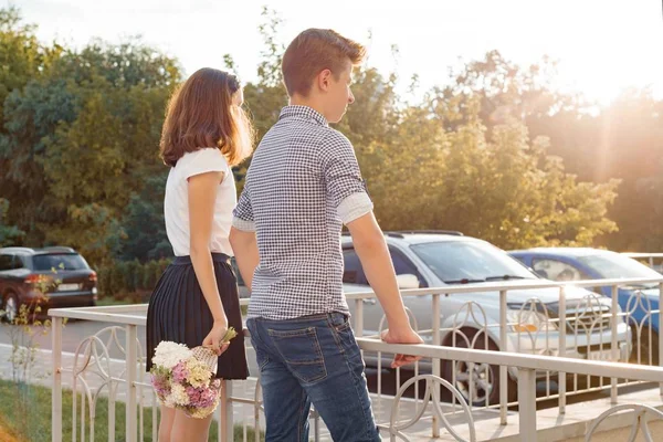 Tonåring unga par pojke och flicka stående rygg, solig sommardag, flicka håller blombukett i handen — Stockfoto