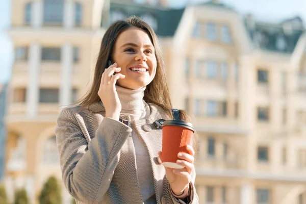 Young smiling beautiful woman walking on the street of a sunny autumn city talking on mobile phone — 스톡 사진