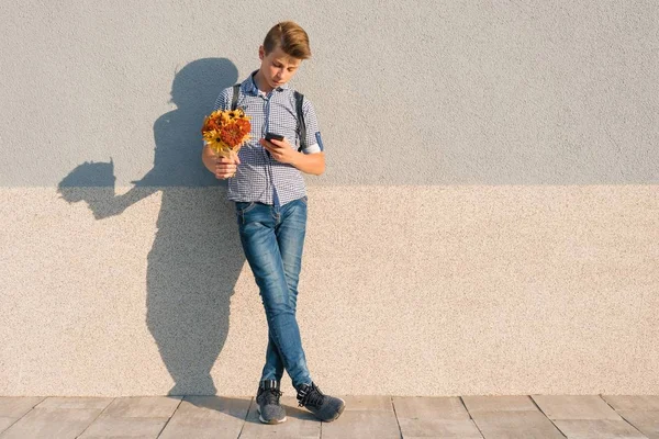 Открытый портрет подростка с букетом цветов, чтение текста на смартфоне, серая стена фоновое пространство — стоковое фото