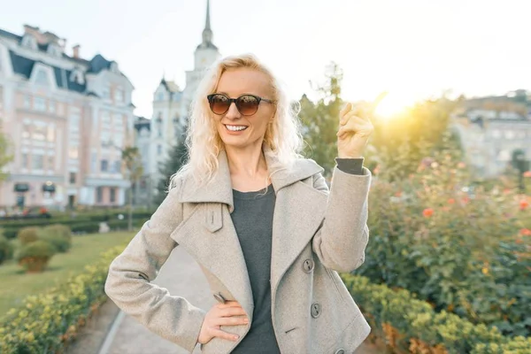 Young smiling woman shows index finger up, attention idea eureka, outdoor background, golden hour
