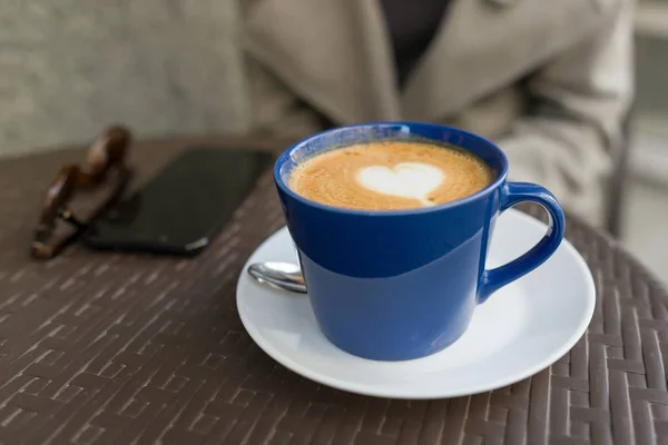 Niebieska filiżanka z cappuccino, na stole w ulicznej kawiarni, rysując serce — Zdjęcie stockowe