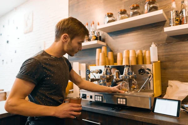 年轻的男性咖啡师在咖啡机附近喝酒。咖啡店经营理念 — 图库照片