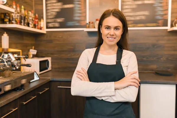 Jovem mulher barista café trabalhador sorrindo olhando para a câmera com os braços dobrados cruzados perto bar contador — Fotografia de Stock