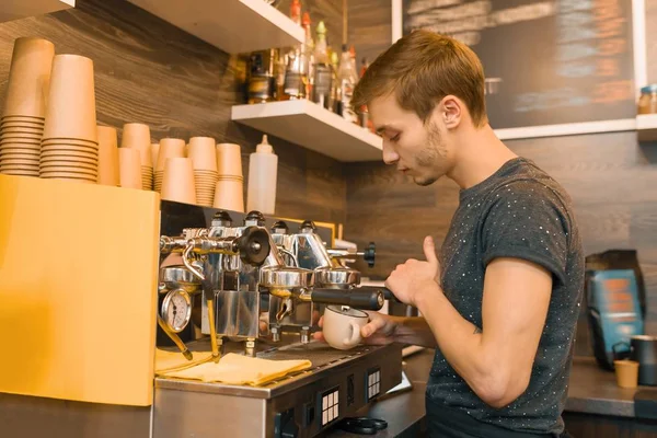 Young male coffee shop worker making coffee with machine