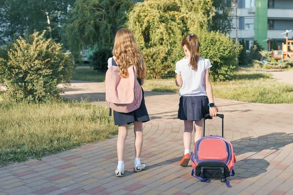 Вид ззаду, дві дівчинки школярки йдуть до школи з рюкзаками — стокове фото