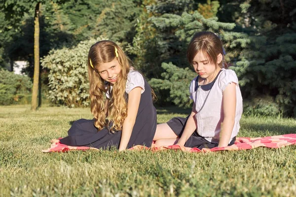 รูปภาพของเพื่อนสาวสองคน อายุ 7 8 ขวบ นั่งอยู่บนหญ้าในสวนสาธารณะ — ภาพถ่ายสต็อก