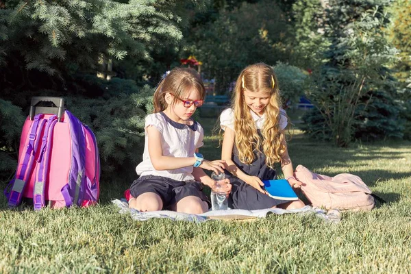 Chicas 7, 8 años en uniformes escolares con mochilas con libros y botellas de agua sentadas en el parque — Foto de Stock