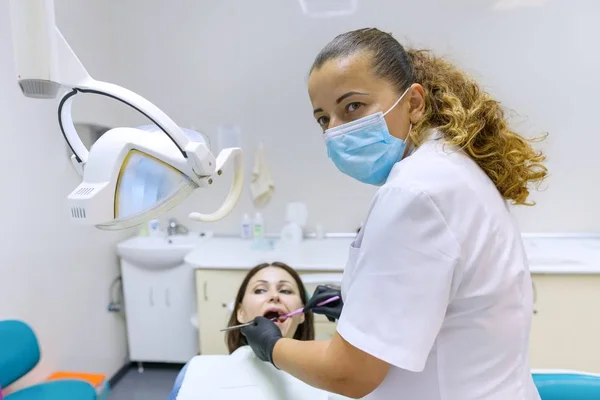 Portret van positieve volwassen vrouwelijke tandarts behandelen patiënt in tandheelkundige stoel. — Stockfoto