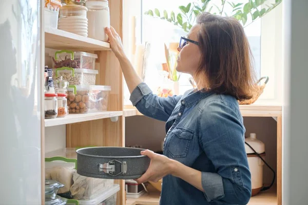 Egy nő a konyhaszekrényben. Tárolóállvány konyhai eszközökkel, a főzéshez szükséges termékek — Stock Fotó