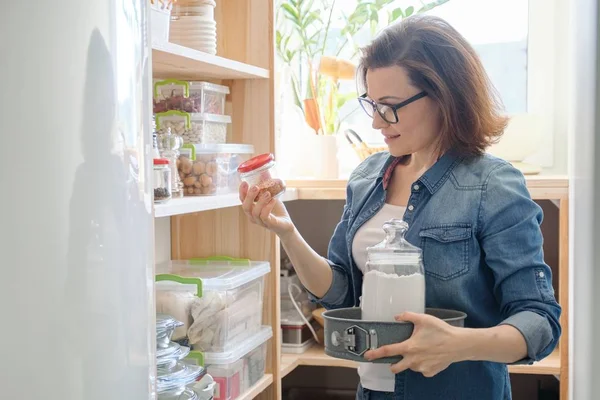 Interiér dřevěné spíži s produkty pro vaření. Dospělá žena s kuchyňského nádobí a jídlem — Stock fotografie