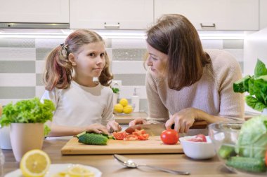 Anne ve kızı mutfakta birlikte yemek sebze salatası, anne ve çocuk gülümseyerek konuşuyor.