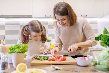 Aile tarafından sağlıklı ev yemeği pişirme. Anne ve kızı salata için mutfakta evde sebze kesti