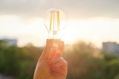 Filament led ampuller, el tutma lambası, akşam gün batımı gökyüzü arka plan